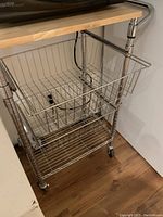 Close-up side view of the microwave stand showing the wooden top, metal frame, and wire basket drawer.