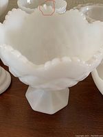 Close-up of milk glass pedestal bowl with chip on rim marked in red.