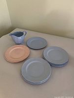 View of all plates stacked in two piles (blue and peach) and milk jug placed alongside.