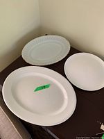 Three white platters shown on table; largest is plain with some speckles.