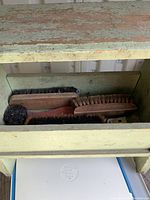 Top view of wooden shoeshine box showing multiple brushes with wooden handles and dark bristles inside.