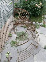 Side view showing the three-tier, semi-circular metal wire shelf with visible rust and wear in an outdoor garden setting.