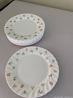 Stack of white dessert plates with multicolored small floral designs around edges, fluted rim
