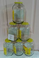Stacked six clear glass jars each with yellow lids. Jars are clean and empty.