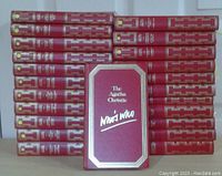 Photo showing 23 hardcover books arranged in two stacks, 22 books with maroon and gold covers stacked in back, 1 book titled 'The Agatha Christie Who's Who' standing in front