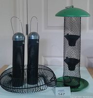 Photo of two niger seed feeders with silver tops and hooks placed inside a circular black metal spider feeder tray, showing design and size.