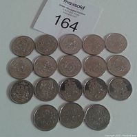 Photo of 18 Canadian half-dollar coins arranged on a white surface, showing the reverse side featuring the Canadian coat of arms.