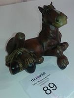 Side angle view of a brown horse figurine laying sideways with visible minor handling marks on the nose and back.