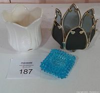 White ceramic candle holder with petal-like rim next to blue textured glass candle holder and brass framed teal glass holder