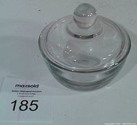 Side view of clear glass candy dish with lid and round knob handle, with auction label nearby.