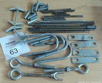 Photo showing various threaded rods, U-bolts, eye bolts, metal plates and toggle bolts arranged on a wooden surface.