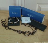 Lia Sophia branded boxes containing necklace and bracelet displayed on wooden surface, showing both items in full view.