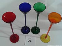 Four long stem colored glasses in red, blue, green, and orange shown together on a white surface with auction number 96 card.