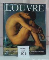 Front cover of the hardcover book with dust jacket, showing classical nude artwork and title 'Louvre'. Seller card with lot number 101 in front.