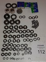 Overview photo of multiple small sealed and open ball bearings, loose bearing parts including races, washers, and balls arranged on a white surface.