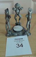 Photo of pewter frog trio tea candle holder with a small tea light candle in the center, showing three standing frogs on decorative base.