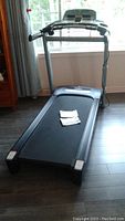 Front view of black and gray Tempo 632T treadmill with running belt and console including owner's manuals on belt.