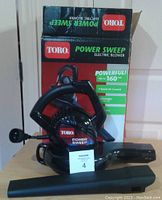 Photo of the Toro Power Sweep electric blower with box and detachable nozzle tubes on a table.