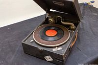 Angled view of the Victrola record player showing the turntable with a record, metal tonearm with sound horn, and open black case.