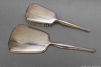 Sterling silver hair brush and hand mirror laid out on gray background, showing front and back sides.