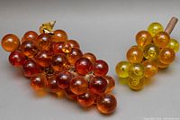 Photo showing both vintage lucite grape clusters, one amber and one yellow-orange, displayed on a light surface.