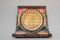 Front view of the SIMPLEX D35 typewriter showing the circular keyboard and worn tin plated body with rust and discoloration.