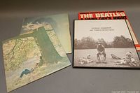 Four vinyl records laid out showing covers of George Harrison's All Things Must Pass, The Beatles A Hard Day's Night soundtrack, John Lennon Plastic Ono Band (rare), and one with tree and person sitting.