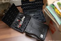 Photo of three black hard plastic carrying cases containing assorted hand tools including sockets, pliers, wrenches, and a portable Coleman butane gas stove inside one case.