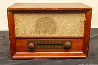 Front view of vintage AM/FM tube radio showing wooden cabinet, fabric speaker grill, and tuning dial with two control knobs.
