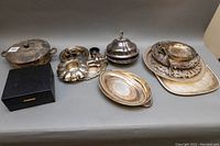 Wide shot showing all silver plated servingware items arranged on table including covered dish, trays, candle holder, and goblet box