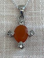 Front view of sterling silver pendant with oval Mexican fire opal and four small clear accent stones on a fabric background.