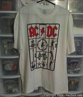 Front view of white AC/DC t-shirt showing red and black graphic design with band logo and icons.