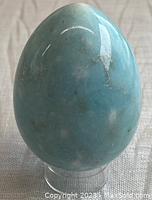 Front view of a polished blue dyed alabaster stone egg on clear stand with visible natural white veins.