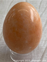 Front view of the peach-colored alabaster stone egg with polished finish on a clear stand