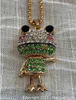 Front view of gold tone frog pendant with multicolored faceted stones, including black eyes and green body. Movable arms and legs visible.