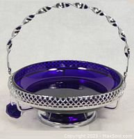 View of round blue cobalt glass dish fitted into chrome metal stand with latticework edge and twisted handle.