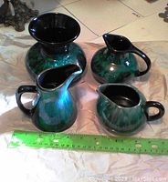 Four Blue Mountain Pottery pitchers with green and black glaze, shown with a ruler for size reference, arranged on a cloth.