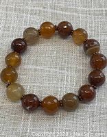 Full view of circular Botswana agate bead bracelet laid flat on textured fabric background, showcasing bead size and color variation.
