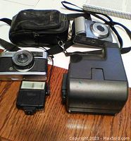 Overview of the lot showing all items: Canon digital camera, Olympus film camera, Polaroid flash, and camera bag.