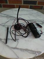 Photo showing the handheld Cobra CB radio with antenna, power cable, and detachable antenna on a marble surface.