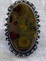 Close-up top view of oval fruit jasper stone ring with decorative silver bezel and patterned band.