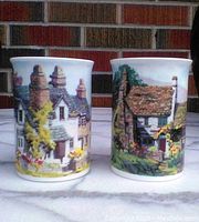 Pair of Lilliput Lane coffee cups from front, showing detailed cottage artwork and white ceramic with colorful painted scenes.