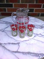 Full set of juice pitcher and three matching glasses with floral designs on a marble surface