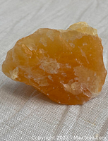 Orange calcite rough chunk from front angle on fabric surface showing translucent orange with white inclusions.