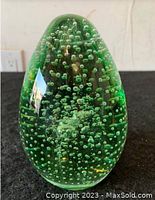 Front view of the green oval glass paperweight showing internal bubbles and smooth glossy finish.