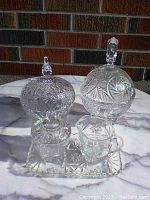 Lot contents showing two footed lidded crystal bowls, sugar and cream set, and tray on a marble surface outside.
