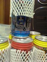 Close-up shot of several pop can containers stacked with visible blue and red labels, all in protective mesh sleeves.