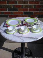 Photo showing 3 cups with matching saucers, 3 dinner plates, and 7 smaller plates arranged on a round marble table.