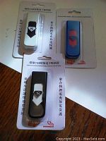 Close-up of three USB rechargeable electronic lighters in original packaging, colors white, black, and blue with red.
