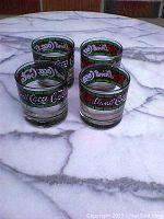 Four vintage Coca Cola glasses displayed on a marble surface showing the stained glass style decoration on the top band.